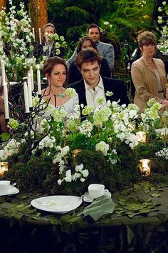 a group of people sitting around a table with flowers and candles on it in front of them