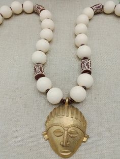 The necklace is approximately 28 inches long. The pendant is made using the lost wax technique.  It is approximately 2.5 inches in width and 3 inches long. The beads are approximately 23 mm round. It is shown on the front and back . The large beads are hand painted African krobo and wooden beads. The beads are a Ivory white and brown. If you have any questions please feel free to contact us at anytime. Keep clear of oils, water and chemicals. Wipe off with soft cloth to clean. The piece is one of a kind. We love to use unique pieces, handmade and carved, from vintage to new. If you have any questions please feel free to contact us at anytime. Our products are not intended for babies or children as we use small pieces, wires and beads. These can be dangerous to them when unsupervised. Gift Traditional White Necklaces With 8mm Beads, Artisan White Necklace With 108 Beads, Symbolic White Jewelry With Round Beads, White Amulet Style Medallion Necklace, Symbolic White Round Bead Jewelry, Symbolic White Beaded Jewelry, Brown Large Beads Necklace For Festival, Spiritual White Jewelry With Wooden Beads, White Wooden Beaded Jewelry For Meditation