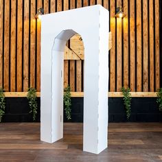 an arch made out of cardboard sitting on top of a hard wood floor next to a wooden wall