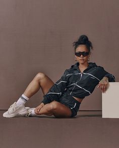 a woman sitting on the ground with her legs crossed, wearing sunglasses and a black jacket