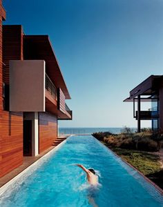 a person swimming in a pool next to a building with wooden sidings on the side