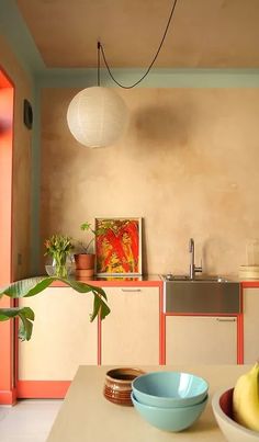 a table with bowls and bananas on it next to a sink in a room that has orange walls