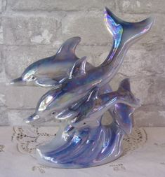 two silver dolphins sitting on top of a table next to a brick wall and white doily