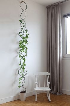 a white chair sitting in front of a window next to a plant on the wall