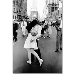 a man and woman kissing in the middle of a street with people walking on either side