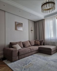 a living room with a large sectional couch in front of a window and a chandelier hanging from the ceiling