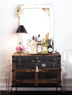 an old trunk is sitting in front of a mirror with bottles on it and a lamp next to it