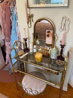 a dressing table with candles, mirror and other items on it in a room filled with clothes