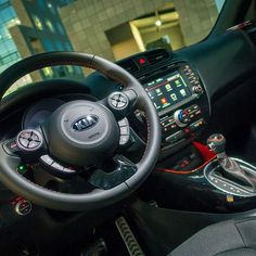 the interior of a car with steering wheel, dashboard and dash lights on display in front of a large building