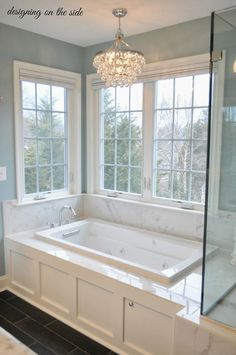 a bathroom with a large tub and two windows in the wall, along with a chandelier