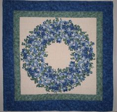 a blue and white quilted wall hanging with flowers on the front, green trim around the edges