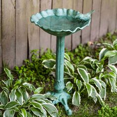 a bird bath sitting on top of a lush green field next to a wooden fence