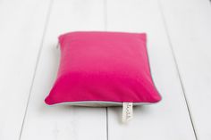 a bright pink pillow on a white wooden floor with a name tag attached to it