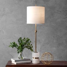 a table with a lamp, vase and books on it in front of a gray wall