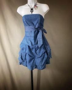 Sweet little strapless denim mini dress in medium wash finish and matching wide sash to wear at waist or at the neck, as shown in photos. Fitted bodice has boning in front for added shaping, waist has horizontal pleating, back panel is smocked with elastic, giving a closer fit. Attached skirt has irregular horizontal rows with pouffed panels for added volume. Invisible side zip closure, fully lined.  Tags still attached. Original retail was $218.00. Fun for Summer, or layered under a black faux/ Casual Strapless Denim Blue Mini Dress, Blue Strapless Cotton Denim Dress, Blue Denim Mini Dress With Ruffles, Blue Denim Strapless Corset, Dark Wash Strapless Denim Mini Dress, Romeo Juliet, Hip Ups, Skirt Mini, Denim Mini Dress