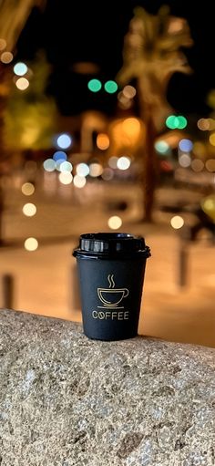 a cup of coffee sitting on top of a stone wall next to a street at night