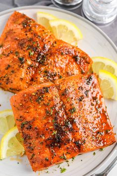 two pieces of salmon on a plate with lemons