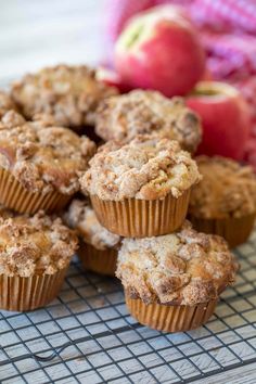 several muffins on a cooling rack with an apple in the background