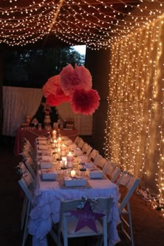 a long table is set up with white chairs and pink pom - poms