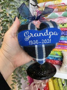 a hand holding up a heart shaped ornament with the name grandpa on it