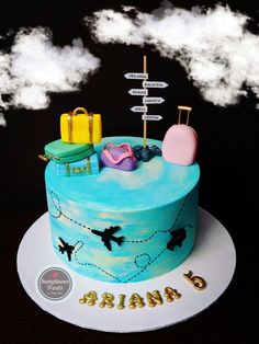 there is a blue cake with luggage on the top and clouds in the sky above it