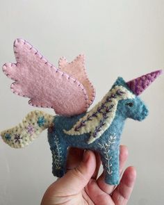 a hand holding a small blue and pink toy horse with wings on it's back