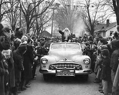 an old black and white photo of a man on top of a car surrounded by people