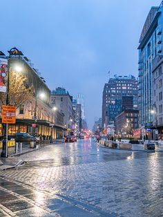 an empty city street at night with cars driving on the road and buildings in the background