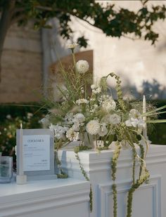 white flowers and greenery are arranged on the mantle