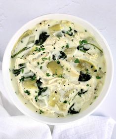 a white bowl filled with soup on top of a white cloth covered in green garnish