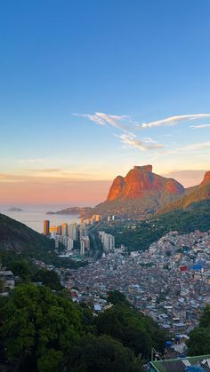 a city with mountains in the background and trees on the foreground, at sunset