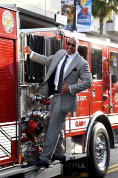 a man in a suit standing on the back of a fire truck