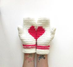 a pair of white knitted gloves with red hearts on them