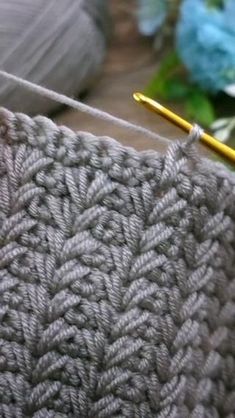 the yarn is being worked on with a yellow knitting needle in front of some blue and white flowers