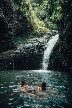 two people in the water near a waterfall