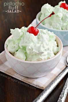 two white bowls filled with whipped cream and cherries on top of a wooden table