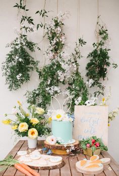 a table topped with a blue cake and lots of greenery next to a sign