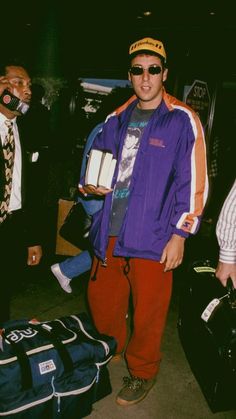 a man standing next to luggage and wearing a purple jacket with an orange stripe on it