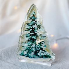 a small glass christmas tree sitting on top of a white cloth covered table next to a lit candle