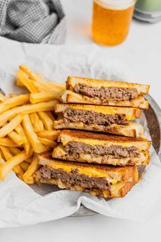 grilled cheeseburger and french fries on a plate with a glass of beer in the background