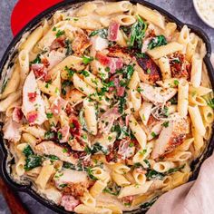 a skillet filled with pasta, meat and spinach on top of a table