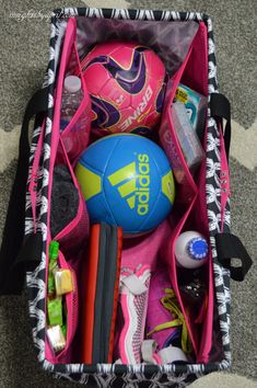 a pink and black bag filled with lots of sports items sitting on the floor next to a carpet