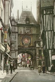 an old photo of people walking down the street in front of buildings with a clock on it