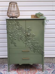 an old dresser painted green with flowers and leaves on the top, next to a lamp