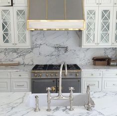 a kitchen with marble counter tops and white cabinets, an oven hood over the stove