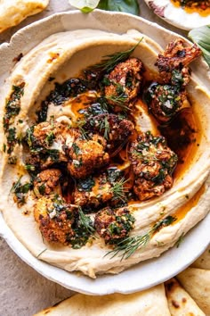 hummus with roasted cauliflower and herbs in a white bowl surrounded by pita chips