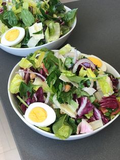 two white bowls filled with salad on top of a gray counter topped with hard boiled eggs