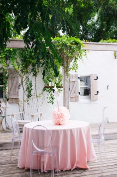 a table with a cake on top of it and chairs around it, in front of some trees