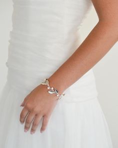 a woman in a white dress wearing a bracelet that has leaves on it and is holding her hand