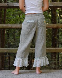 a woman standing in front of a fence with her back to the camera, wearing high waist pants and white tank top